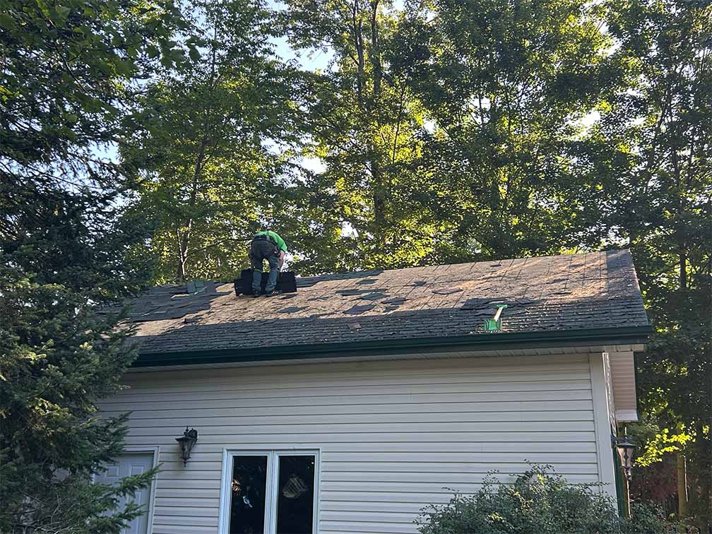 Roofing contractor removing old asphalt shingles during roof replacement