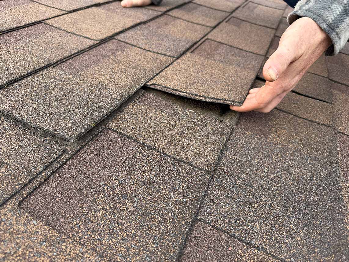 Close-up of asphalt shingles being lifted during a professional roof inspection in Ottawa