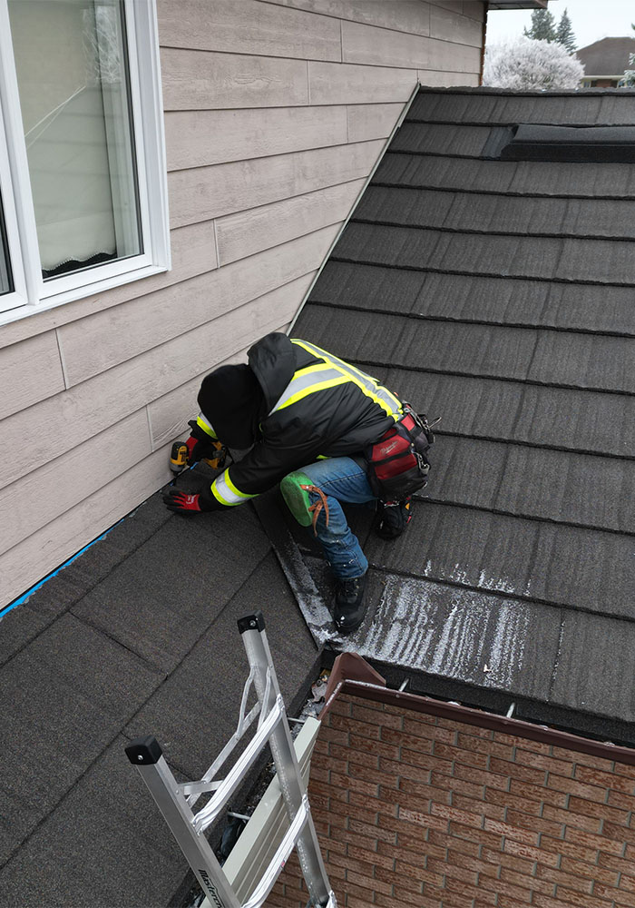 roofing technician repairing flashing on asphalt shingle roof near exterior wall