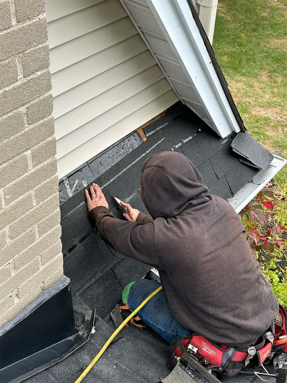 roofing contractor repairing asphalt shingles near wall flashing on residential roof