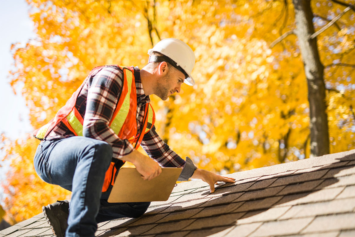 roofing professional inspecting asphalt shingles on residential roof for damage and wear