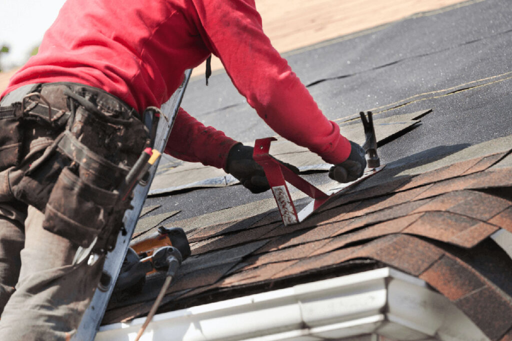 contractor repairing damaged asphalt shingles on residential roof to fix leak